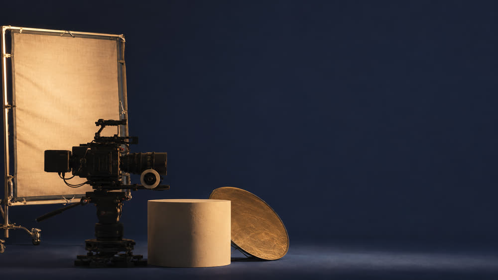 A cinema camera and gold reflector standing before a deep navy cyclorama in the Valcourt film studio.